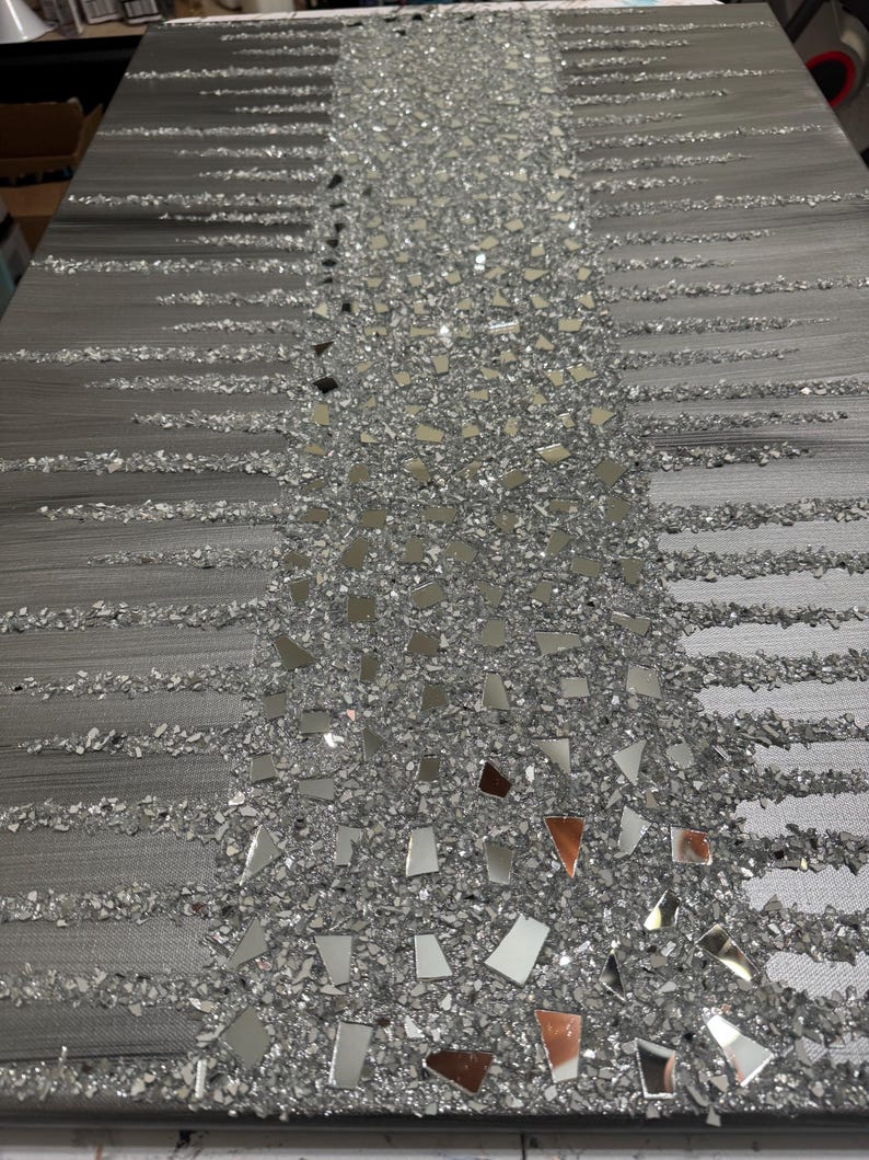 May include: A grey canvas wall art featuring a vertical design of silver glitter and small mirrored pieces. The glitter and mirrored pieces are arranged in a cascading pattern.
