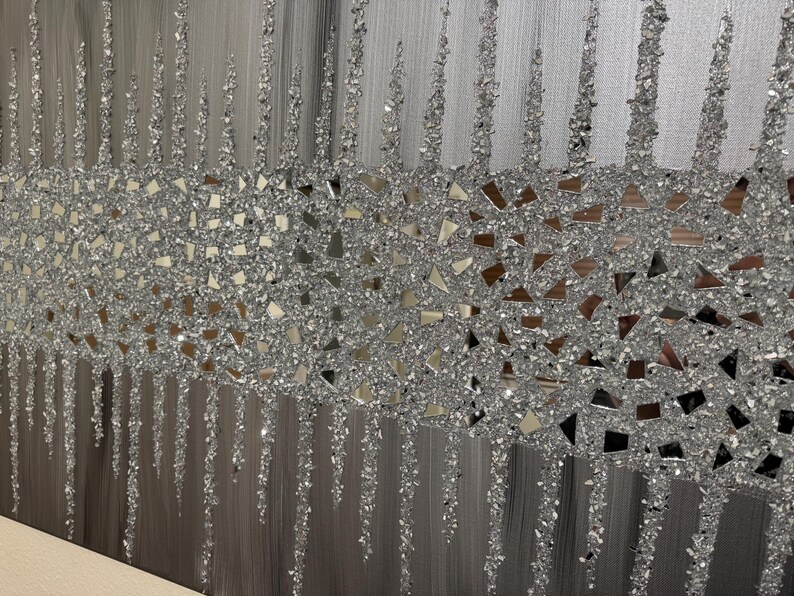 May include: A silver and grey abstract wall art piece with a textured, glittery finish. The art features a band of silver glitter and small mirrored pieces.