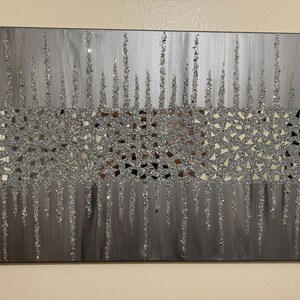 May include: A silver and grey abstract wall art piece with a glittery finish. The art features a mosaic of small, mirrored pieces in the centre, with vertical lines of glitter extending from the mosaic.