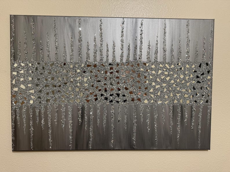 May include: A silver and grey abstract wall art piece with a glittery finish. The art features a mosaic of small, mirrored pieces in the centre, with vertical lines of glitter extending from the mosaic.
