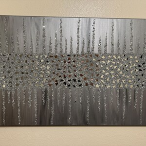 May include: A silver and grey abstract painting with a textured glitter finish. The painting features a band of small, mirrored squares in the centre.