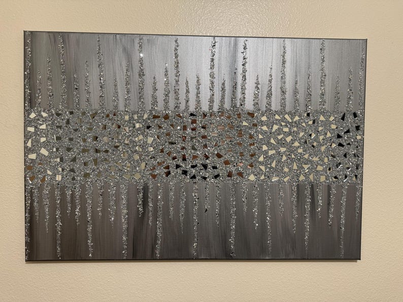 May include: A silver and grey abstract painting with a textured glitter finish. The painting features a band of small, mirrored squares in the centre.