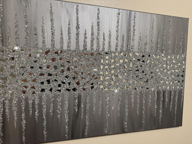 May include: A silver and grey abstract wall art piece with a glittery texture. The art features a band of silver glitter with a mosaic pattern, and a background of vertical silver lines.
