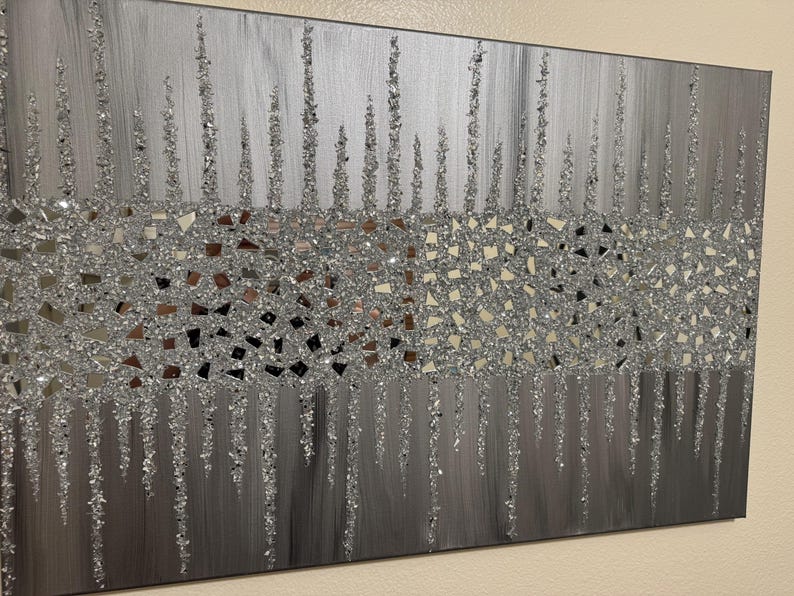 May include: A silver and grey abstract wall art piece with a textured glitter finish. The art features a design of vertical lines with a band of small, irregular silver shapes.