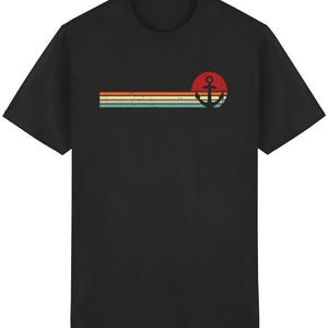 Könnte beinhalten: Schwarzes T-Shirt mit Retro-Design. Es zeigt einen roten Kreis mit einem schwarzen Anker und drei horizontale Streifen in Orange, Gelb und Türkis. Das Design hat einen Vintage- und Used-Look.