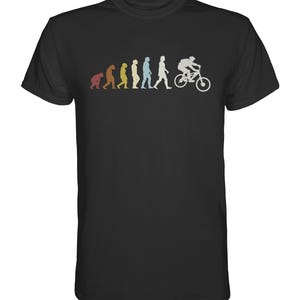 Può includere: T-shirt nero con una grafica umoristica dell'evoluzione umana, che culmina con una persona in bicicletta. Le fasi dell'evoluzione sono raffigurate in marrone, giallo, blu e bianco. Il ciclista è su una bicicletta.