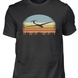 May include: Black t-shirt featuring a retro design of a glider silhouetted against a sunset. The graphic includes a blue, yellow, and orange gradient sun with a forest at the bottom. A stylish tee for aviation enthusiasts.