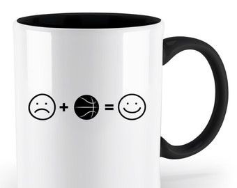 May include: White ceramic mug with a black rim and handle. The mug has a black graphic of a sad face, plus sign, basketball, equals sign, and a smiley face. The text reads "Sad + Basketball = Happy".