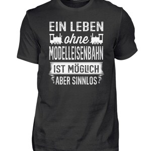 May include: A dark grey t-shirt with white text that reads "Ein Leben ohne Modelleisenbahn ist möglich aber sinnlos". The text is surrounded by two small train engine graphics.