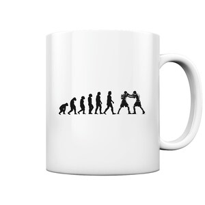 May include: White ceramic mug with a black silhouette image of the evolution of man, ending with two boxers in a fighting stance.