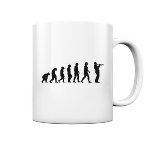 Könnte beinhalten: Weiße Keramiktasse mit einer schwarzen Silhouette der Evolution des Menschen, die mit einem Mann endet, der Trompete spielt.