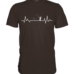 Könnte beinhalten: Braunes T-Shirt mit weißer Grafik, die eine Herzschlaglinie mit einem Fischer beim Auswerfen einer Leine darstellt. Der Fischer ist in den Herzrhythmus integriert und schafft ein einzigartiges Design.