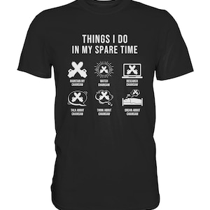 Op de afbeelding: Zwart T-shirt met witte tekst die "Things I do in my spare time" luidt. De tekst wordt omringd door zes pictogrammen van kettingzagen met verschillende acties, waaronder het onderhouden, het bekijken, het onderzoeken, het praten over, het nadenken over en het dromen over kettingzagen.