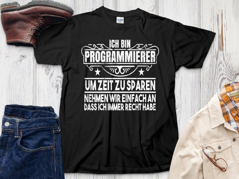 May include: Black t-shirt with white text that reads "ICH BIN PROGRAMMIERER UM ZEIT ZU SPAREN NEHMEN WIR EINFACH AN DASS ICH IMMER RECHT HABE." The shirt is displayed with a pair of blue jeans, a brown boot, and a plaid shirt.