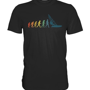 Peut inclure: T-shirt noir avec un motif rétro représentant l'évolution humaine vers le windsurf. Le design utilise une palette de couleurs arc-en-ciel, allant de l'orange au bleu en passant par le jaune et le vert. Un design sportif et amusant.