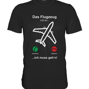 Könnte beinhalten: Schwarzes T-Shirt mit einem weißen Flugzeug-Motiv und dem Text "Das Flugzeug ruft an... ...ich muss geh'n!" Das Flugzeug ist als Telefon mit grünen und roten Knöpfen dargestellt, die mit "Annehmen" und "Ablehnen" beschriftet sind.