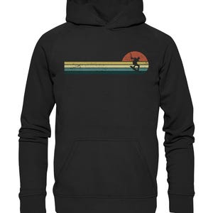 Könnte beinhalten: Schwarzer Hoodie mit einer Retro-Grafik einer Person beim Wakeboarden vor einem Sonnenuntergang.