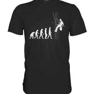 Könnte beinhalten: Schwarzes T-Shirt mit einem weißen Aufdruck, der die menschliche Evolution zeigt und mit einer Person endet, die an Seilen hängt und einen Farbeimer hält. Das Design zeigt humorvoll die Entwicklung zum Maler.