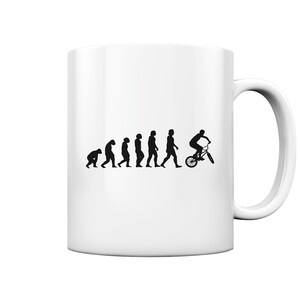 Può includere: Una tazza in ceramica bianca con una silhouette nera dell'evoluzione dell'uomo, che termina con una persona che guida una bicicletta BMX. Il testo "Evolution of a BMXer" è stampato sulla tazza.