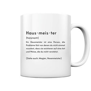 Könnte beinhalten: Weiße Keramiktasse mit schwarzem Design, das das Wort "Hausmeister" als eine Person definiert, die Probleme löst, von denen man nicht einmal wusste, dass sie existieren. Der Text enthält die deutsche Aussprache des Wortes und einen Hinweis, dass es einem Magier oder Zauberer ähnelt.