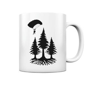 Könnte beinhalten: Weiße Keramiktasse mit einer schwarzen Silhouette eines Fallschirmspringers, der über drei Kiefern mit einem einzigen Wurzelsystem schwebt.