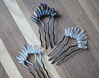 May include: Two sets of hair combs with crystal accents. One set has iridescent crystals and the other has clear crystals. The combs are black and have a wavy design.