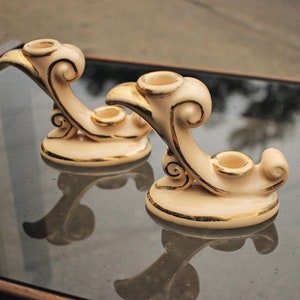 Puede incluir: Dos candelabros de cerámica blanca con detalles dorados. Cada candelabro tiene un diseño de espiral y dos portavelas.