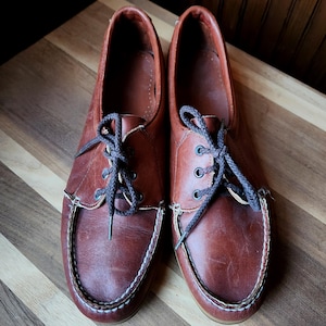 May include: A pair of brown leather lace-up shoes with a white stitching detail around the edge. The shoes are tied with dark brown laces.