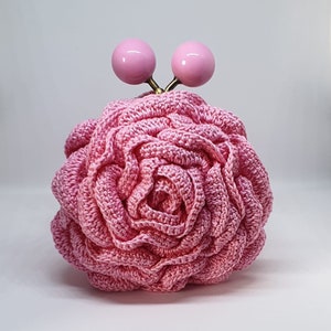 May include: A pink crocheted rose-shaped purse with two pink ball-shaped clasps. Color: Pink.