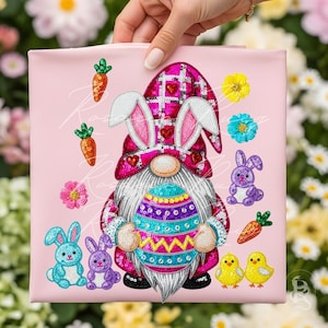 Könnte beinhalten: Rosa dekoratives Kissen zum Thema Ostern mit einem Zwerg, der Hasenohren trägt und ein dekoriertes Ei hält. Das Kissen ist mit Karotten, Blumen, Küken und Hasen verziert. Der Hut und das Ei des Zwergs sind mit Pailletten verziert.