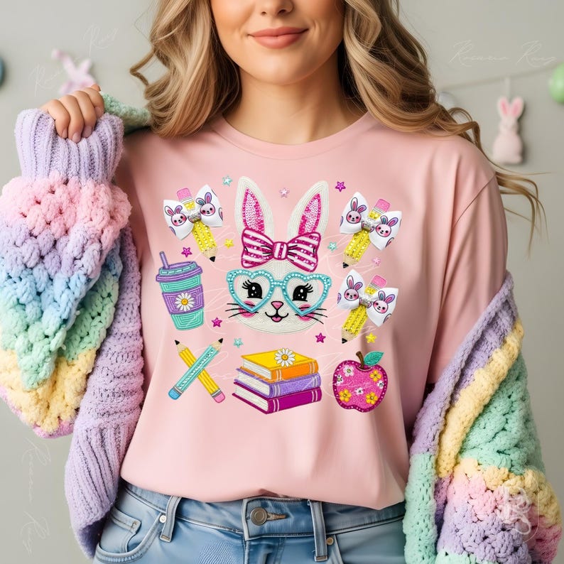 Puede incluir: Camiseta rosa claro con un conejito de dibujos animados con gafas y pajarita, rodeado de l&aacute;pices, libros y lazos. El conejito tiene gafas en forma de coraz&oacute;n. La camiseta forma parte de una colecci&oacute;n con tem&aacute;tica de primavera o Pascua.