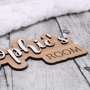 May include: A wooden sign with the text "Sophie's Room" in white lettering. The sign is made of light brown wood and has a slightly distressed look.
