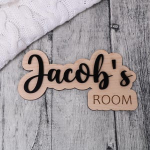 May include: Wooden sign with the text "Jacob's Room" in black lettering. The sign is made of light wood and has a rustic look.