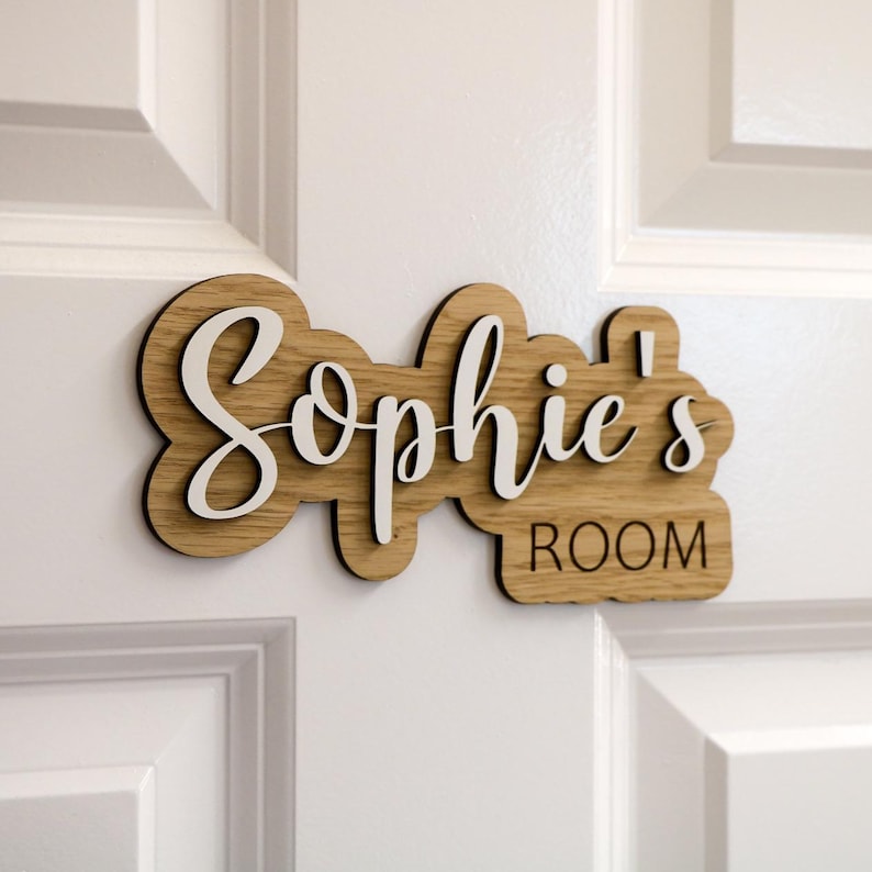 May include: A wooden door sign with the name "Sophie's Room" written in white cursive lettering.