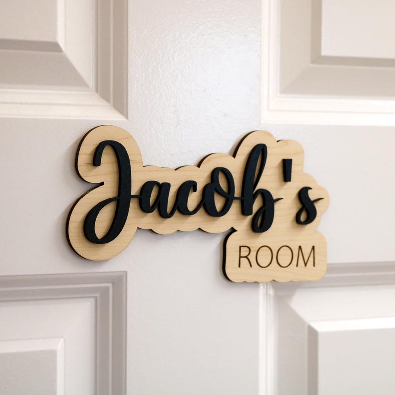 May include: A wooden door sign with the text "Jacob's Room" in black lettering. The sign is made of light wood and has a slightly curved shape.