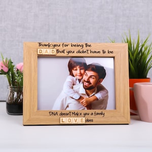May include: A wooden photo frame with a picture of a father and son hugging. The frame has the text "Thank you for being the DAD that you didn't have to be" and "DNA doesn't make you a family LOVE does" with the words DAD and LOVE spelled out with wooden letter tiles.