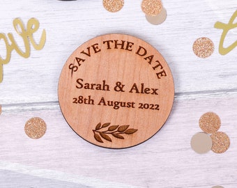 May include: Round wooden save the date magnet with a twig design. The magnet says "Save the Date" with the names "Sarah & Alex" and the date "28th August 2022".