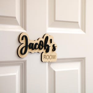 May include: Wooden door sign with the name "Jacob's Room" in black lettering.