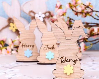 Op de afbeelding: Drie houten konijnen-kaartjeshouders met de namen Harry, Jack en Darcy. Elk konijn heeft een klein bloemetje in een andere kleur.