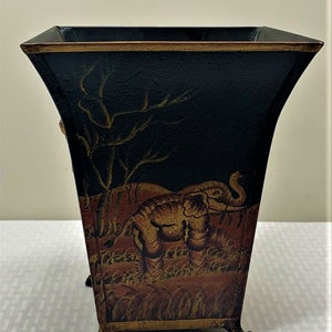 May include: Black metal planter with gold accents and an elephant design. The planter has four feet and a square opening.