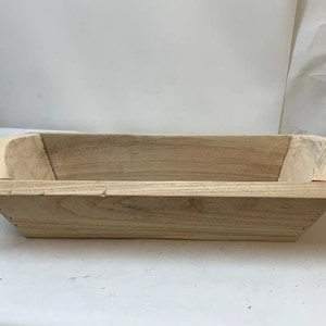 May include: A natural wood rectangular trough planter with rounded edges. The planter is made of unfinished wood and has a rustic look.