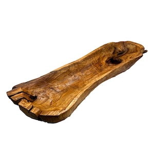 May include: A long, hand-carved wooden bowl with a natural, organic shape. The bowl is made from a light brown wood with darker grain patterns and a smooth, polished finish. The edges are uneven, showcasing the wood's natural form.