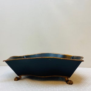 May include: A black metal tray with gold trim and four gold feet. The tray has a wavy edge and is perfect for serving or displaying items.