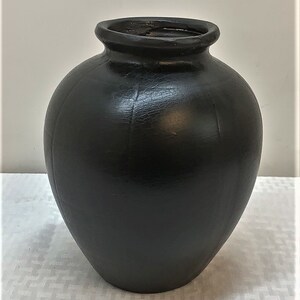 May include: A black ceramic vase with a rounded body and a wide opening. The vase has a textured surface.