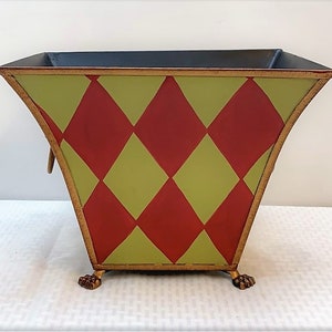 May include: A decorative metal planter with a diamond pattern in red and green. The planter has gold accents and sits on three gold feet.