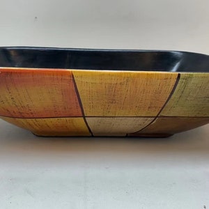 May include: A square ceramic serving bowl with a black rim and a geometric pattern of orange, yellow, and green squares.