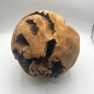 May include: A spherical, decorative wooden sculpture with a natural, organic aesthetic. The sculpture is a warm, light brown color with a rough, textured surface and several irregular openings. The wood grain is visible, adding to its rustic charm.