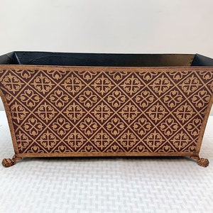 May include: A rectangular planter with a dark brown base and gold patterned design. The planter has four decorative feet.