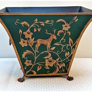 May include: Green metal planter with gold trim and decorative deer and floral design. The planter has a square top and rests on four claw feet. The interior is dark blue.
