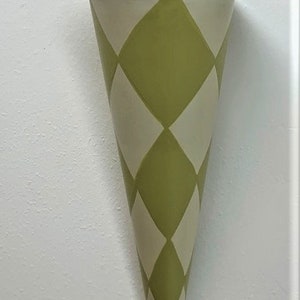 May include: A green and white diamond patterned metal cone-shaped vase with a gold rim. The vase has a hook on the top for hanging.